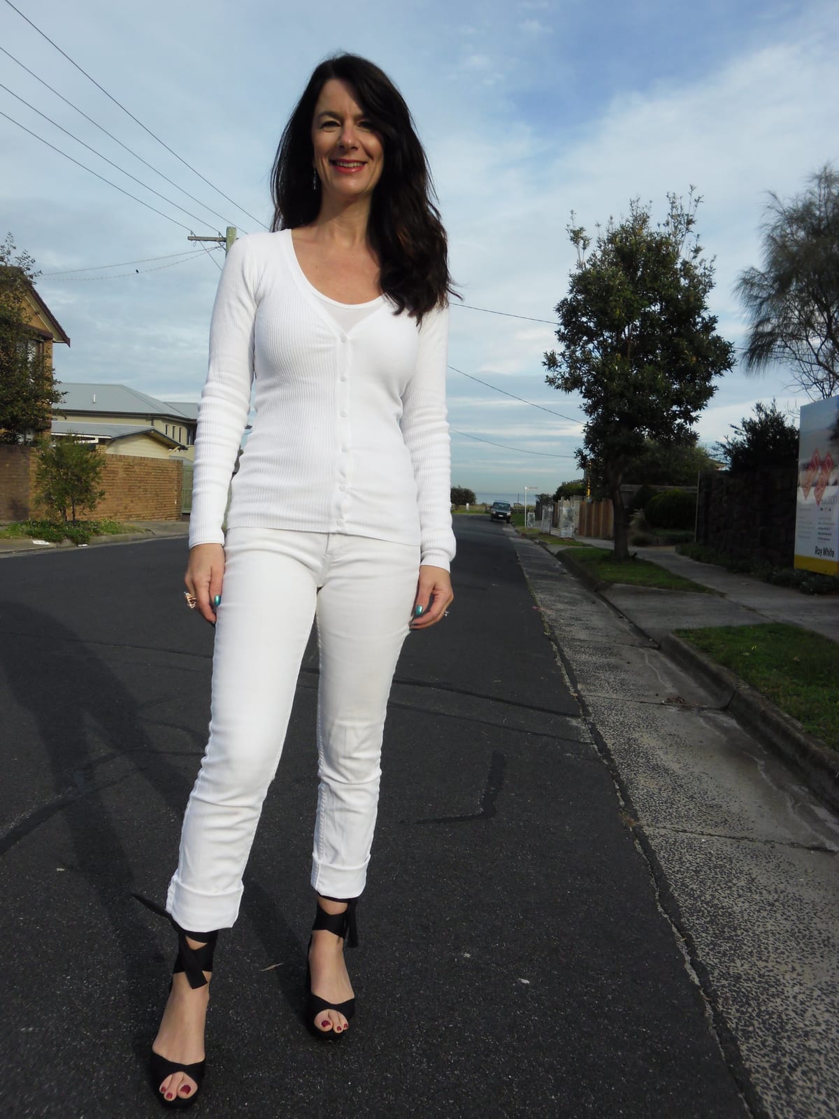 Ribbed white long-sleeved top over a white camisole with white jeans and black heeled sandals