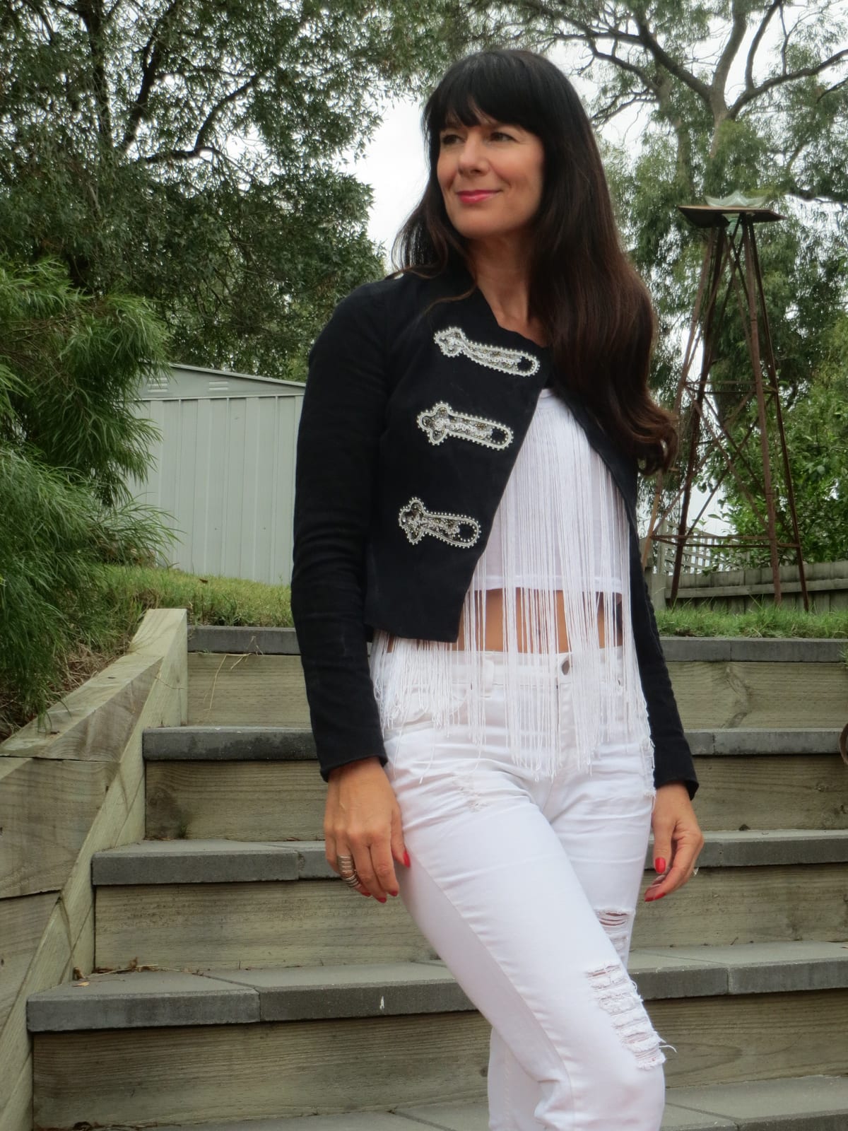 White fringed crop top with white ripped jeans under a black military jacket with silver embellishment