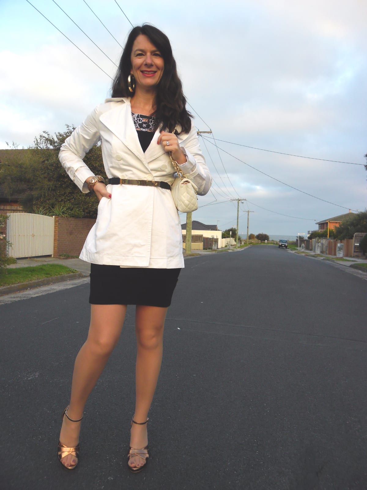 Belted white trench coat worn over a black mini skirt with rose gold strappy heels